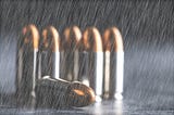 Six bullets with casings, five standing and one on its side, on a gray surface with a black background, in a heavy rain
