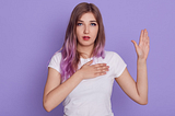 A photo of a young woman with her right hand on her heart and her left hand raised as though making an oath.