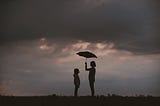 A girl holds an umbrella above her and a friend.