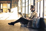 man sitting on floor with laptop open on his lap