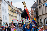Picture of the pride parade in munich, people holding a large giraffe stuffed animal in the air celebrating pride.