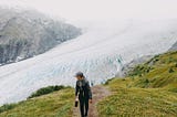 Lone individual, hiking uphill with a magnificent Alaskan glacier backdrop.