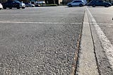 Close up of a strip of concrete in the asphalt parking lot with newer store in the background