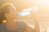 A girl drinking a bottle of water with sun rays shining from the background.