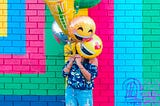 A young girl covering face with smiley balloons with colourful and vibrant background.