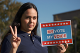 A young Latina woman makes a peace sign with her right hand and holds a sign in her land hand that reads “My Vote, My Voice.”