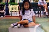 Small girl sitting on platform in park.