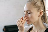 A blonde woman using her fingers to plug one nostril as she breathes in a yogic alternate nostril breathing pattern.