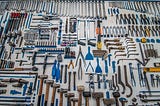 A vast array of hundreds of carefully placed hand tools, wrenches, mallets, pliers, saws, drillbits, etc. sprawls across a clean, solid, light-colored background.