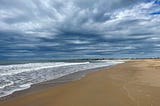 Sand, ocean, and an expansive cloudy sky.