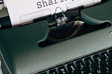 An antique typewriter with a white piece of paper in it that says the word SHARING