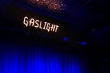 a blue curtain with the words “Gaslight” in neon over top