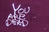 Crawford Jolly took this photo of handwritten words spray painted on a plum-colored wall saying, “You Are Dead.”