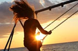 Image of a woman riding a swing at sunset