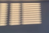 Sunlight filtered through window blinds falling across a blank wall.