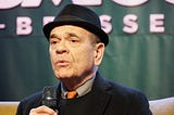 Robert Picardo, wearing a hat and holding a microphone.