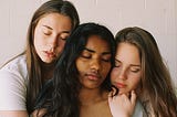 Three young women hugging, eyes closed. Photo from the shoulders up.