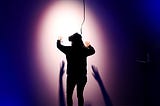 Person with a Virtual Reality headset gesturing in front of a wall, illuminated by a spotlight.