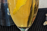 Amber liquid in a champagne glass with a lemon peel floating in it