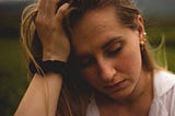 A woman sits, resting her head on her hand, looking depressed.