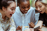 Fun group of three women looking surprised and excited by what they see on a phone
