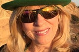 A head shot of Gloria Lesher in a green hat and sunglasses
