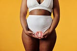 black woman in plain under garments holding a grapefruit in front of her privates