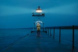 Person holding an umbrella on a pier near a lighthouse