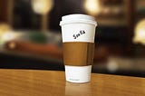 A standard Starbucks-style coffee cup to-go with a thin, insufficient-seeming band of brown cardboard wrapped around the white cup to protect the buyer’s hands. On the cup itself, someone wrote with black sharpie “Soulla”. Near the very bottom of the cup are some printed letters: “it’s hot, stupid”; truly groanworthy.