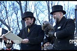 Screencap of the Groundhog Day live feed from Gobbler’s Knob featuring two men in black coats and top hats, one holding a groundhog and one a small scroll