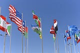 Multinational flags waving in the wind under a blue sky.
