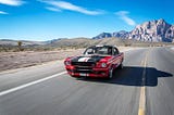 2 individuals enjoying a red Ford Mustang on an open country road