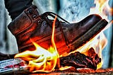 A rugged brown timberland steps on an old newspaper on fire