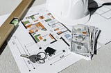 Building plans with some cash, house keys, a level, and a hardhat.