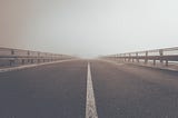 A concrete road under a gray sky leading into unknown