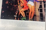 Photo of the band ‘JungK’ taken in NYC in 1998. There are four girls in the band dancing in brightly colored clothes and several photographers are taking their photo in a large room with a floor-to-ceiling window behind them.