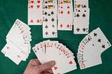 Four hands of cards on a green felt tablecloth — one, at the bottom, is being held by a player; the ones on either side are fanned out, and the one at the top is separated into four piles by suit.