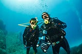 two divers diving underwater with rock corals