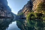 A narrow river gorge in France surrounded by high cliffs. The cliffs are lit on one side by a low sun, and sark on the other.