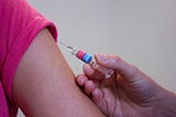 Syringe about to be used to inject vaccine into upper arm or patient.