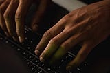 A dark hand typing away on a keyboard