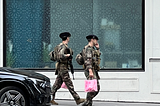 Two soldiers carrying machine guns and pink shopping bags.