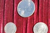 3 silver coins, heads side facing up, a quarter and 2 dimes totaling forty-five cents are in a pyramid formation laid on burgundy velvet fabric