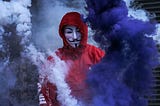 A person in a red jumpsuit wearing an anonymous mask.