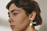 Woman wearing silver earrings with a single AirPod dangling from it.