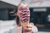 Mulher oferecendo um sorvete de cor framboesa na casquinha. Imagem por Liam Shaw no Unsplash.