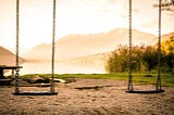 Two empty swings hanging side by side at sunset. Evoking a sense of absence, memory, and quiet reflection.