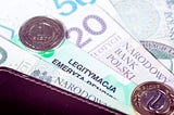 Na zdjęciu widoczne są polskie banknoty 20 i 50 złotych, monety oraz legitymacja emeryta-rencisty częściowo schowana w portfelu. Całość przywołuje skojarzenia z poczuciem finansowego wsparcia i bezpieczeństwa, jakie może zapewniać dodatek dopełniający. Zestawienie pieniędzy oraz dokumentu emerytalnego budzi wrażenie stabilności i spokoju, płynących z posiadania środków na codzienne potrzeby.