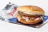 Photo of a Sonic Junior Deluxe Burger. The burger is wresting on top of its wrapper with a plain white background.