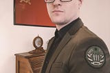 This photo is of Jason L. Hamilton in an olive green suit (with olive green “SRA” patch) amidst his desk & a Soviet flag.